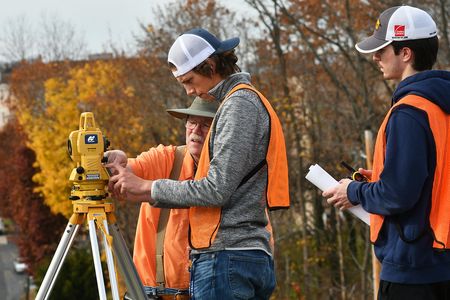 A professor showing two students how to utilize surveying equipment in fall in West Virginia. 